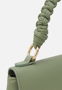 Borsa a mano in pelle verde con manico intrecciato, dotata di ferrature dorate e texture liscia, che mostra un design angolare.