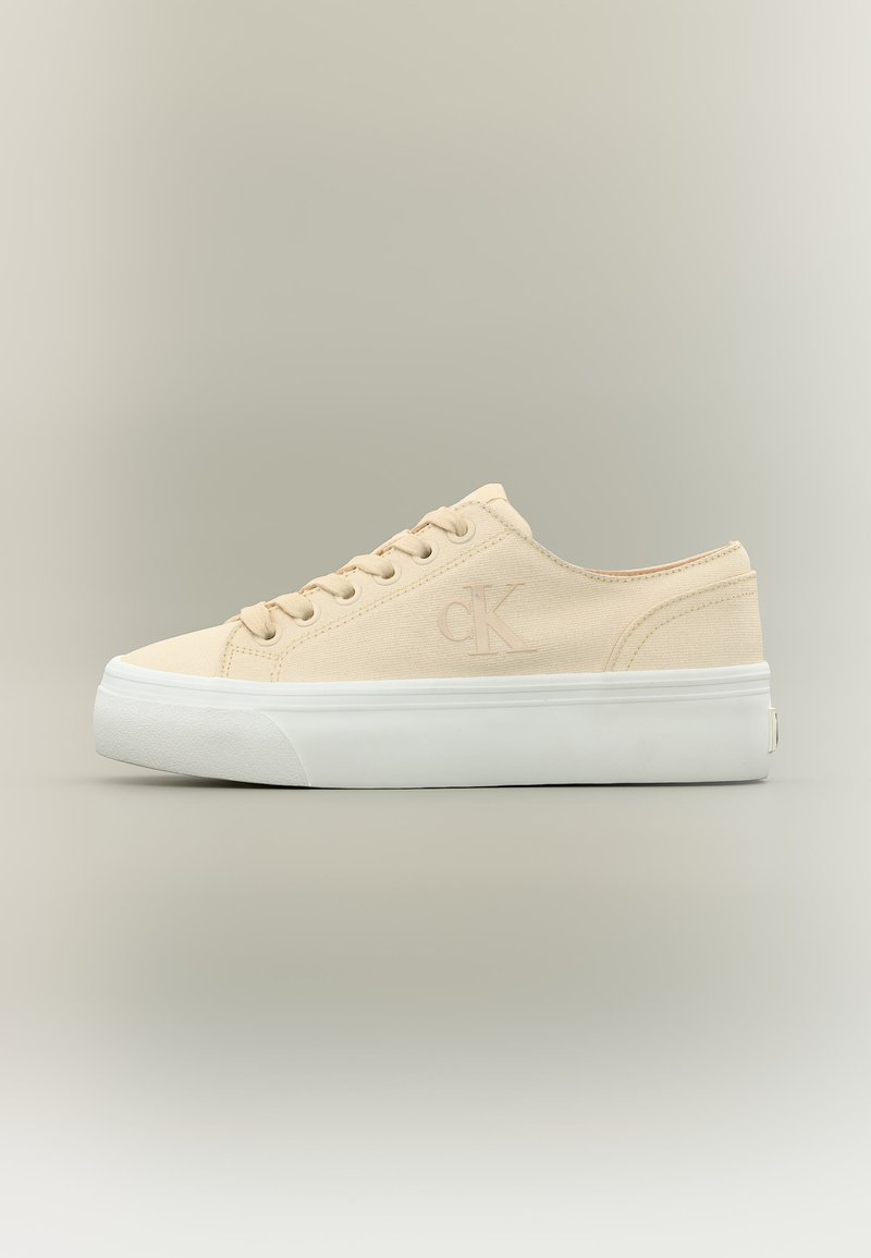 Μπεζ καμβάς χαμηλού προφίλ αθλητικό παπούτσι με λευκή παχιά ελαστική σόλα και διακριτικό λογότυπο «CK» στο πλάι.