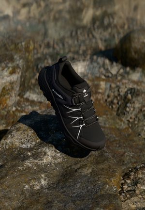 Black waterproof Columbia shoe with gray accents, laces featuring elastic bands, textured outsole, designed for outdoor activities.