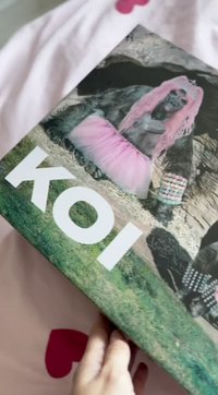 Bokomslag med "KOI" i hvit tekst; bildet viser en gorilla med rosa hår, iført en rosa tutu og mønstrede tilbehør, satt mot en gressbakgrunn.