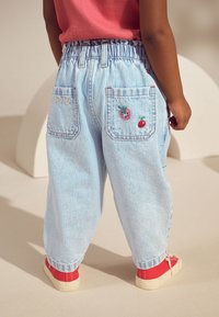 Šviesiai mėlynos dryžuotos medvilninės kelnės su elastinga liemene, su dviem kišenėmis nugaroje, puoštos siuvinėtomis braškėmis ir gėlėmis. Raudoni batai.