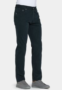Pantaloni in cotone blu scuro con design a gamba dritta, dotati di tasche anteriori e zip. Abbinati a sneakers grigie basse.