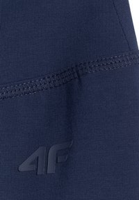 Gros plan sur un tissu bleu marine avec des coutures renforcées et un logo de marque 4F en relief sur une surface textile texturée.
