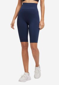 Shorts da ciclismo blu navy a vita alta con tessuto testurizzato, lunghezza a metà coscia e vestibilità aderente. Abbinati a scarpe da ginnastica bianche.