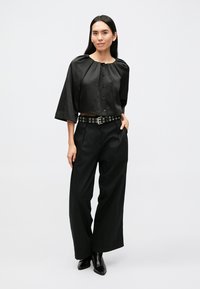 Top in raso nero con scollo rotondo, maniche corte e chiusura con bottoni. Abbinato a pantaloni neri a vita alta, a gamba larga, e una cintura con borchie.