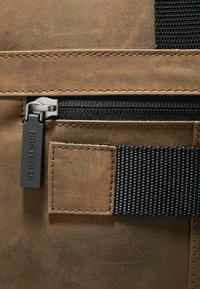 Borsa in pelle marrone con superficie testurizzata, dotata di zip e tracolla nere. Accenti cuciti evidenziano i scomparti e i dettagli.