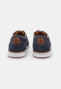 Navy blue leather shoes with brown leather accents, rounded shape, white rubber soles, and perforated detailing on the back.