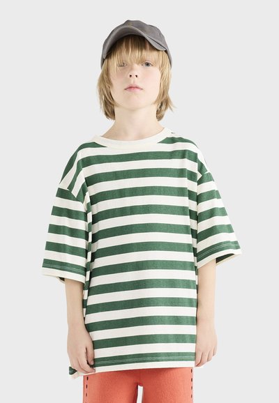 Zielono-biały t-shirt w paski z krótkimi rękawami, okrągłym dekoltem, wykonany z miękkiego materiału. Noszony z pomarańczowymi spodniami i szarym czapką.