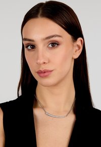 Collana d'argento con un pendente curvo decorato da una fila di gemme scintillanti, montata su una delicata catena, esposta su un modello contro uno sfondo neutro.