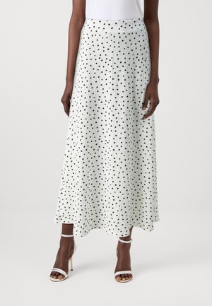 White maxi skirt with black polka dots, textured fabric, pleated design, and a flat waistband. Paired with strappy high-heeled sandals.