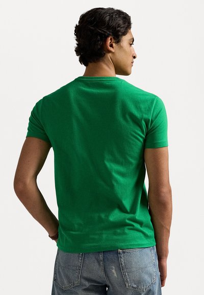 T-shirt de algodão verde com decote redondo e mangas curtas, apresentando uma textura suave e um design ajustado, combinado com jeans azuis.