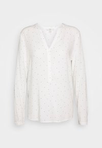 Weiße Bluse mit langen Ärmeln, V-Ausschnitt und Knopfleiste, die mit schwarzen Punkten gleichmäßig über den Stoff verteilt ist. Glatte Textur.