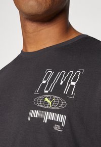 Camiseta de algodón negra con un estampado gráfico de la palabra "PUMA" en blanco y amarillo, con un diseño de un globo y un código de barras en el centro.