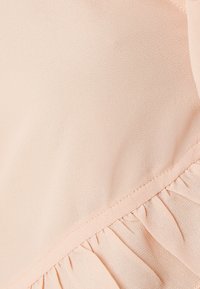 Light pink fabric with a smooth texture features ruffled detailing along the hem, showcasing a subtle sheen and delicate stitching.