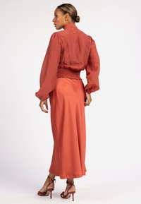 Roestoranje blouse met pofmouwen en smocktail, gecombineerd met een bijpassende lange rok. Soepele textuur, enkel-lang, en sleehakken.