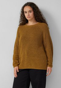 Mosterdgele gebreide trui met een ribbeltextuur, ronde halslijn en lange mouwen. Gecombineerd met donkere zwarte broek, minimalistisch ontwerp.
