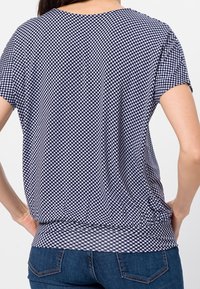 Top s modrým a bílým károvaným vzorem gingham, krátké rukávy, zaoblený výstřih a volný střih, vyrobený z měkké, lehké látky.