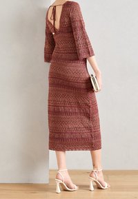 Robe midi à motifs rouges avec un dos décolleté et des manches trois-quarts. Associée à des sandales à talons blanches et une pochette métallique.