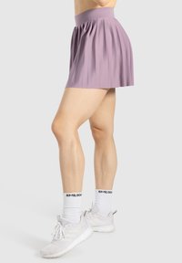 Gonna plissettata viola con una cintura larga, realizzata in un tessuto leggero, abbinata a scarpe da ginnastica bianche e calze con motivi.