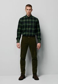 Groene en zwarte geruite overhemd met twee borstzakken, gecombineerd met donkergroene corduroy broeken en bruine veterschoenen.