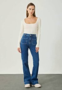 Lichtgekleurde geribde longsleeve top gecombineerd met hoge taille blauwe jeans met een uitlopende pijp en twee achterzakken. Zachte textuur.