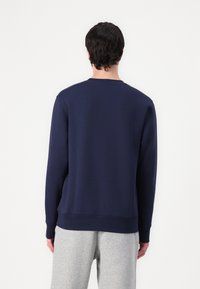 Marineblauwe sweatshirt met lange mouwen, ribgebreide manchetten en zoom, gladde textuur, gedragen over lichtgrijze sweatpants tegen een witte achtergrond.