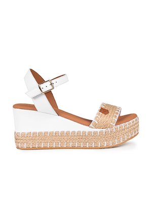 Sandalia wedge blanca con correa ajustable en el tobillo, material de yute trenzado alrededor de la suela y plantilla color tostado. Presenta un detalle de correa texturizada y trenzada.