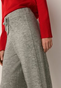 Grå strik-sweatpants med en tekstureret overflade, snøre i taljen og ribbede sidehenfald, parret med en rød ribbet sweater.