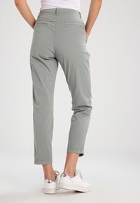 Jasnoszare, krótkie spodnie z gładkiego, elastycznego materiału, z bocznymi kieszeniami i dopasowaną talią, zestawione z białymi trampkami.