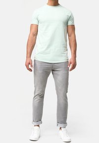 Minttu vihreä lyhythihainen paita, miehustakaulus, yhdistettynä vaaleanharmaisiin kapeneviin housuihin, taitetut hihansuut ja valkoiset lenkkarit. Yksinkertainen ja moderni muotoilu.