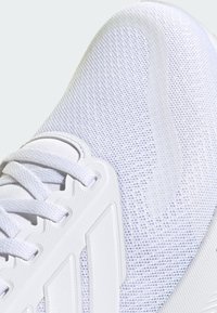Scarpa sportiva bianca con tomaia in rete traspirante, dettagli testurizzati, lacci piatti e una suola in gomma resistente con scanalature orizzontali.