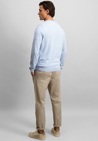 Lyseblå genser med rund hals, ribbestrikkede mansjetter, kombinert med beige bukser og lyse sneakers. Enkel design, myk tekstur.