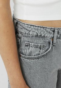 Pantalon en denim gris avec une finition texturée, comportant une poche avant standard, des passants de ceinture et une fermeture à bouton. Détails de couture visibles.