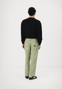 Black sweatshirt, light green denim pants with two back pockets, and black sneakers with white stripes. Simple design, solid colors.