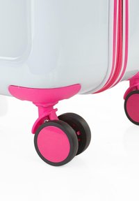 Maleta rígida en blanco con acentos en rosa. Cuenta con dos ruedas rosas y una cremallera a juego. Textura suave y diseño compacto.