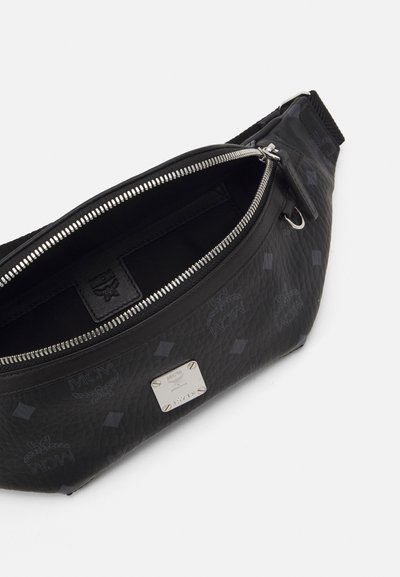 Borsa in vita MCM in pelle nera testurizzata con zip argentata, motivo logo e placca metallica del marchio, mostrata parzialmente aperta su sfondo bianco.