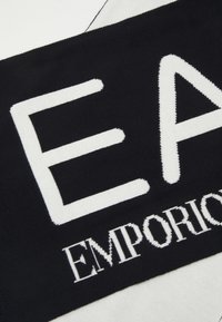 Țesătură neagră cu litere albe din tricotare "EA" și "EMPORIO" expuse proeminent. Textură netedă, tipografie îndrăzneață.