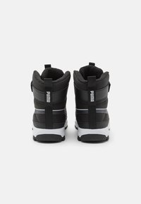Zwarte wandelschoenen met een gevoerde kraag, gestructureerde materialen, een reflecterende streep en een witte rubberen zool. Heeft een opvallend logo op de achterkant.