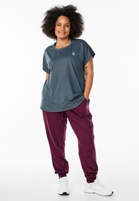 T-shirt sportivo grigio con colletto rotondo e maniche corte, abbinato a pantaloni tapered bordeaux. L'outfit è realizzato in un tessuto morbido e leggero.