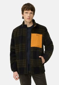 Fleecejacke mit einem schwarz-grünen Karomuster, ausgestatt mit einer orangen Brusttasche, einem kontrastierenden Reißverschluss und einem Stehkragen-Design.