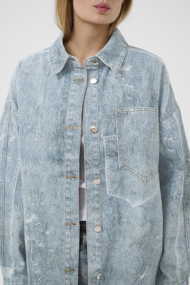 Veste en denim oversize bleu clair avec texture usée, boutons argentés et une poche poitrine. Elle présente un col classique et une coupe ample.