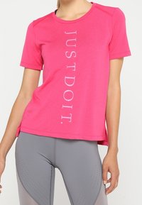 Rosa träningsskjorta med korta ärmar, med vertikalt vitt text "JUST DO IT" på framsidan; slät tyg, avslappnad passform.