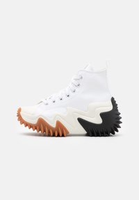 Höga sneakers med ett vitt textilöverdrag, en tandad svart och brun gummisula och silverögon för snörningen. Texturerad design med unik form.