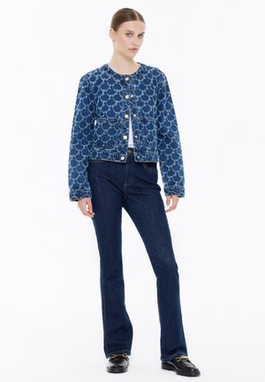Blaue Denimjacke mit strukturiertem Muster, Rundhalsausschnitt und Knopfverschluss. Kombiniert mit dunkelblauen, weit geschnittenen Jeans und schwarzen Schuhen.