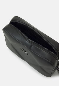 Borsa in pelle nera con chiusura a zip; presenta una texture trapuntata e scomparti interni; logo in argento sulla parte anteriore; forma rettangolare compatta.