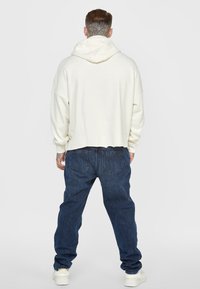 White cropped hoodie with a drawstring hood, paired with loose dark blue jeans and white sneakers. Features relaxed fit and ribbed cuffs.