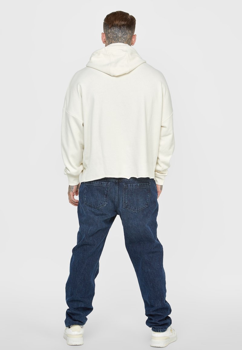 White cropped hoodie with a drawstring hood, paired with loose dark blue jeans and white sneakers. Features relaxed fit and ribbed cuffs.