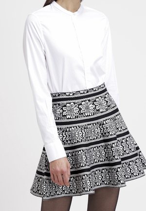 Weißes langärmeliges Knopfhemd kombiniert mit einem schwarz-weiß gemusterten, geblümten ausgestellten Rock, der aus strukturiertem Stoff mit mehrlagigem Design gefertigt ist.