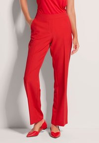 Rote maßgeschneiderte Hose aus glattem Stoff mit geradem Bein und einem weichen Bund. Kombiniert mit passenden roten Ballerinas.