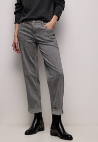 Grå mønstrede bukser med en tekstureret finish, optrukket kant og sidelommer, kombineret med sorte ankelstøvler med en gulddetalje.